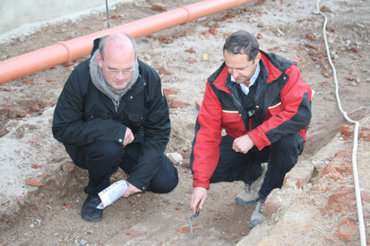 Dr. Thomas Westphalen (links) und Matthias Rummer (rechts) vom Landesamt für Archäologie Sachsen begutachten Reste des erhaltenen Fußbodens im ehemaligen Gebäudeinneren.