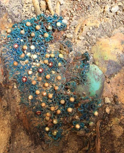 Zarte Grabbeigabe: Eine Netzhaube aus Filigrandraht, verziert mit Perlen und mit zu kleinen Blumen zusammengesetzten roten Schmucksteinen. 