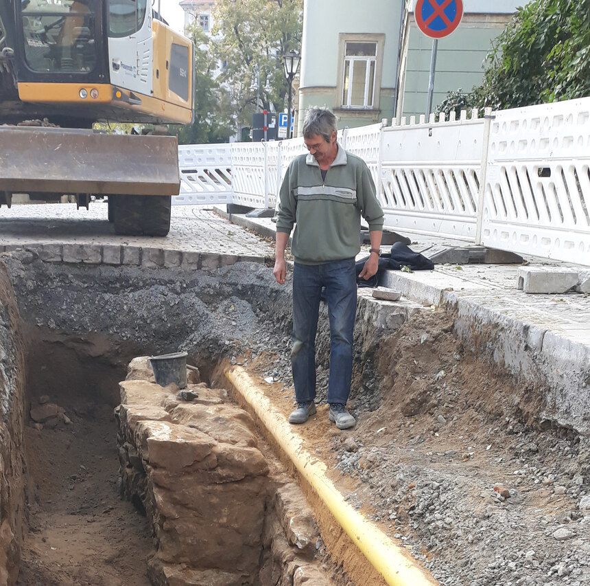 Herr Mario Steinbach steht rechts neben einer freigelegten Mauer in der Oberen Burgstraße in Pirna. Im Hintergrund ist ein Bagger zu sehen.