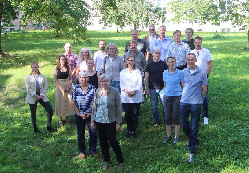 Auf dem Bild sind die 20 Teilnehmerinnen und Teilnehmer des Treffens der Projektarbeitsgruppe ArchaeoTin zu sehen. Sie stehen unter Bäumen im grünen Innenhof des LfA Sachsen