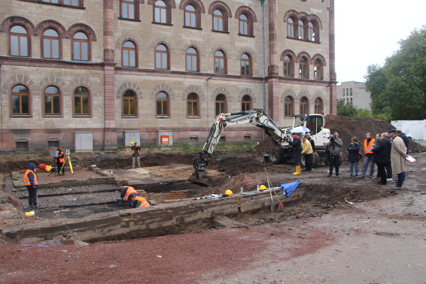 Medienvertreterinnen und -vertreter stehen neben den archäologischen Grabungen vor dem Zwickauer Amtsgericht.