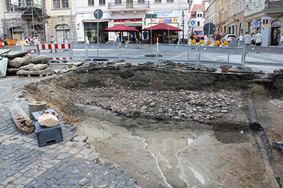 Flächige Reste der Marktpflasterung des 13./14. Jahrhunderts werden hier durch eine frühneuzeitliche Wasserleitung aus Holz geschnitten.