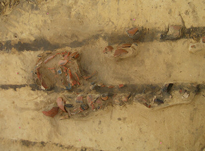 Archäologische Dokumentation eines Urnengrabes: Deutlich ist die Zerstörung des Befundes durch die dunklen Pflugspuren zu erkennen.